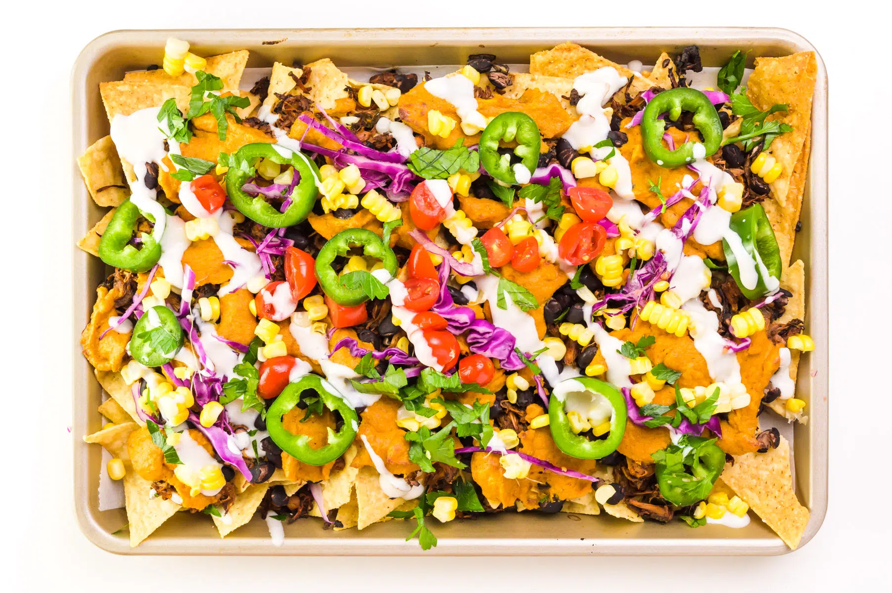 Looking down on a baking dish loaded with jackfruit nachos. It's drizzled with sour cream on top.