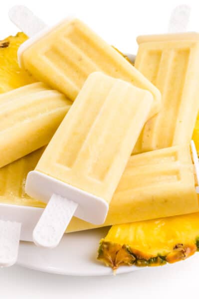 A plate of pineapple popsicles has sliced pineapple wedges on it too.