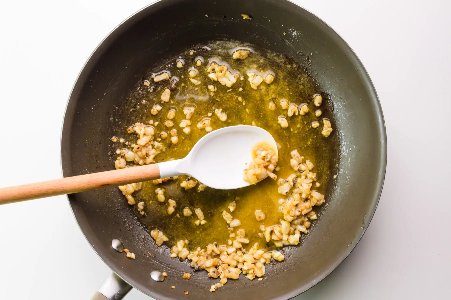 A spatula is stirring onions and garlic in a skillet with flour.