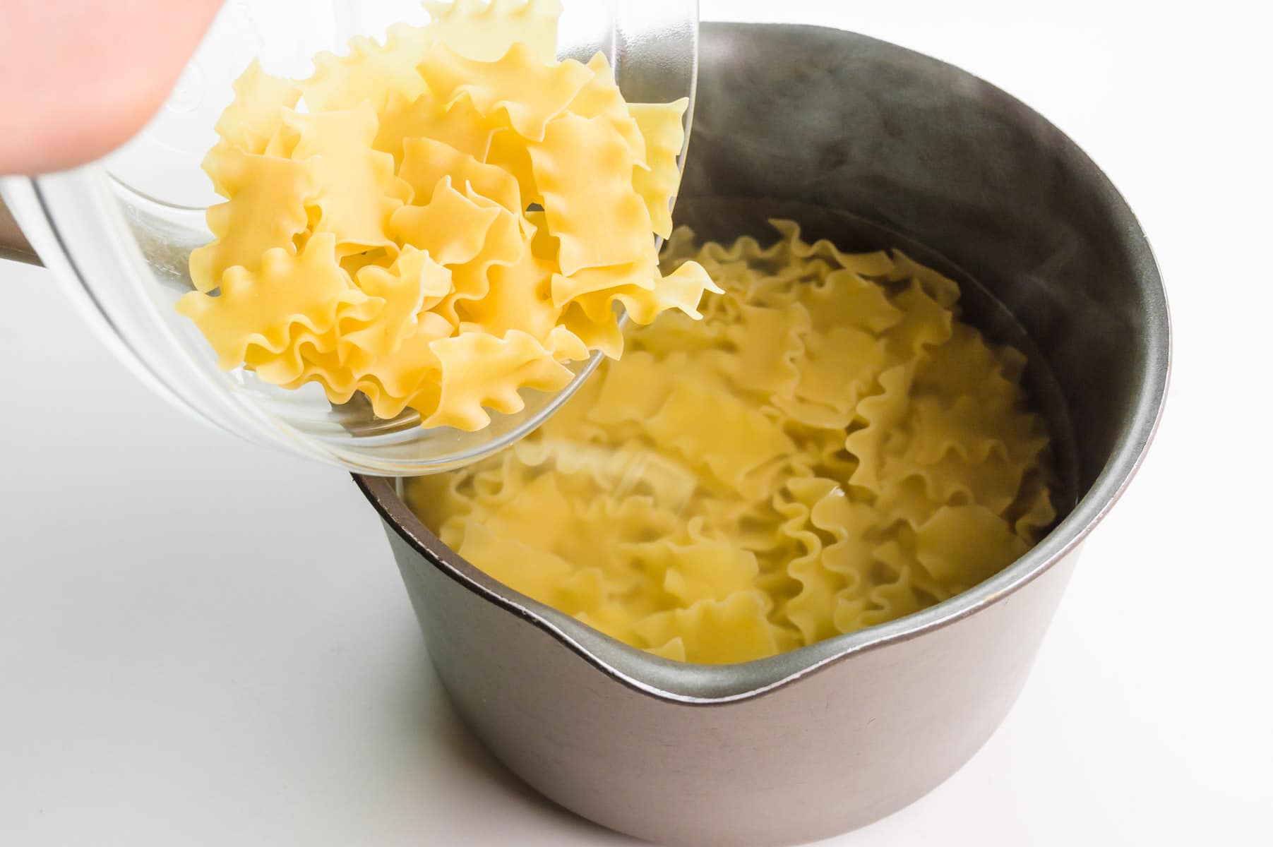 Noodles are being added to boiling water in a saucepan.