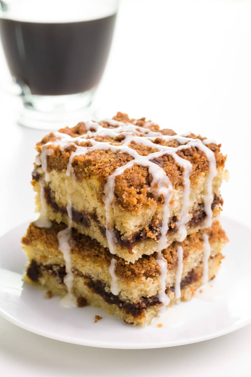 A stack of two slices of vegan coffee cake sits in front of a cup of coffee.