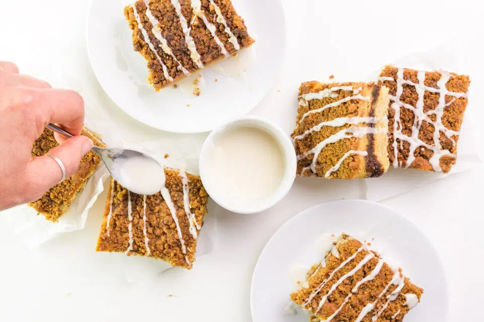 A hand drizzles icing on slices of coffee cake.