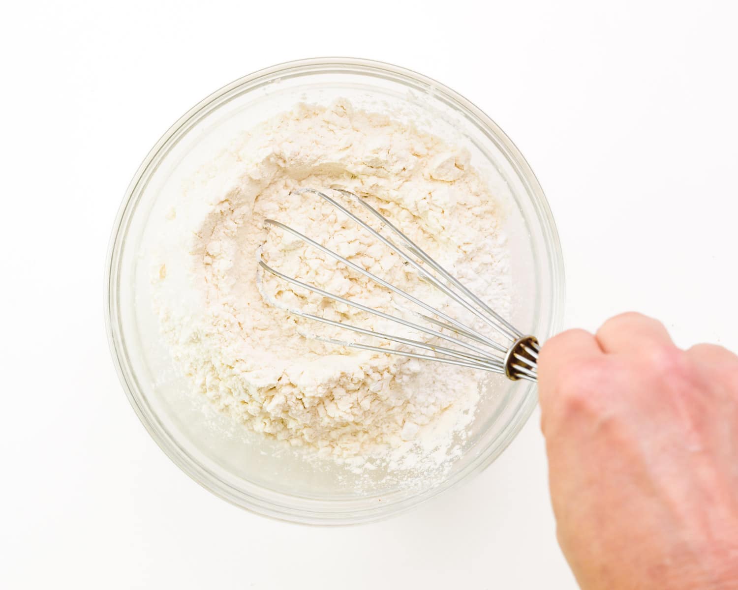 A hand holds a whisk, stirring a flour mixture.