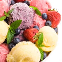 A large bowl holds dishes of different dairy-free frozen yogurt, such as berry, pineapple, and strawberry.