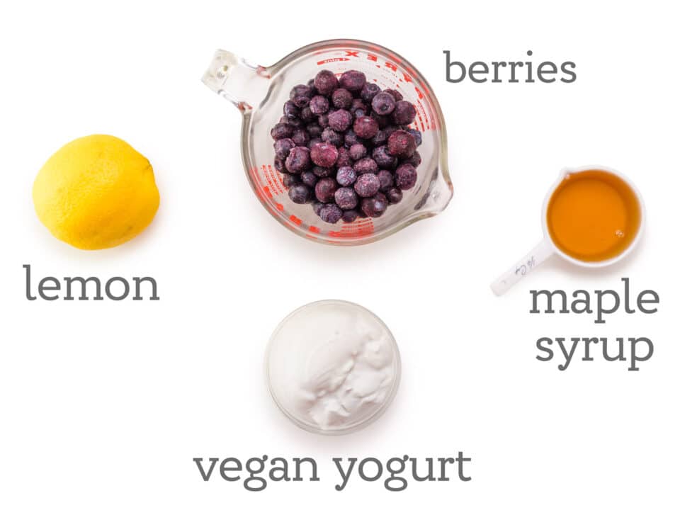 Ingredients are laid out on a white table. The labels next to them ready, berries, maple syrup, vegan yogurt, lemon.