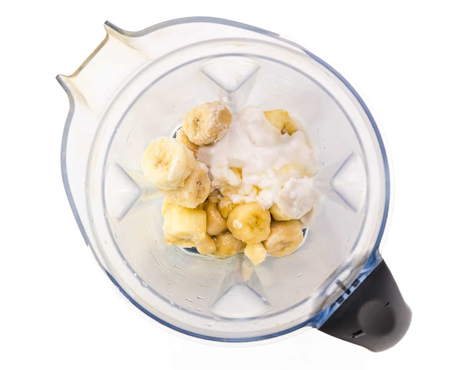 Frozen bananas and vegan yogurt are in the bottom of a blender.