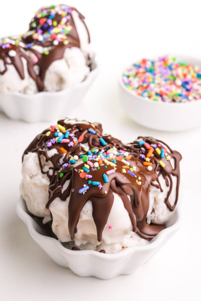 Two bowls of ice cream with chocolate magic shell topping and sprinkles.  A sprinkle bowl sits in the background.