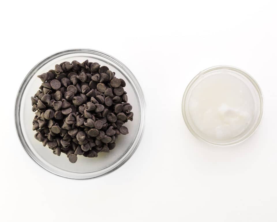 A bowl of chocolate chips and coconut oil sits on a white counter.