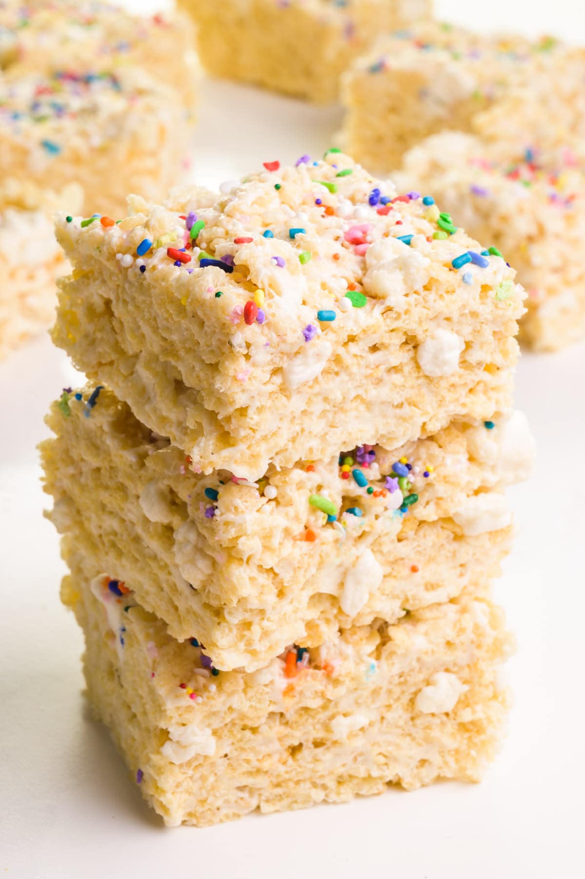A stack of vegan rice krispie treats sits in front of other foods in the background.