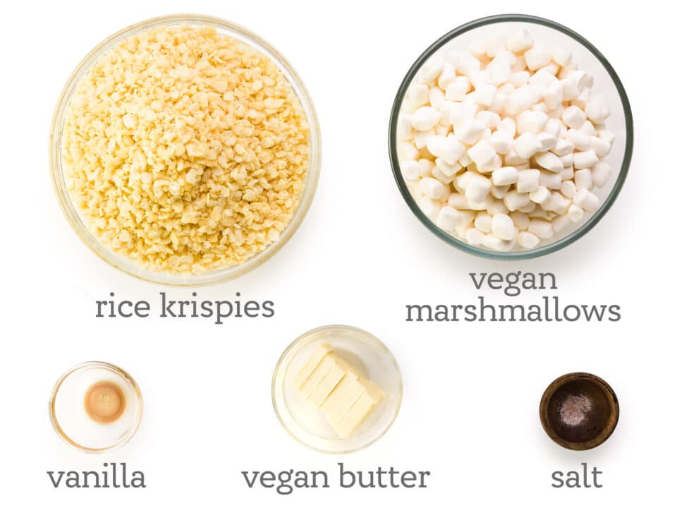 Ingredients are laid out on a white table, including Rice Krispies, vegan marshmallows, salt, vegan butter, and vanilla.