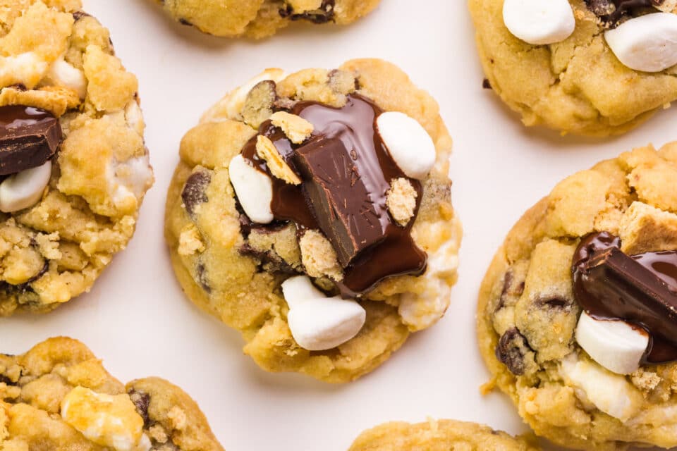 Looking at a cookie with other cookies around.  Each cookie contains chocolate chunks and marshmallows.