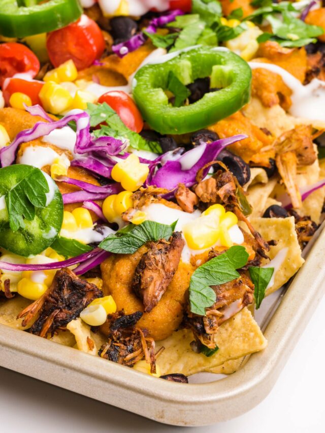 A baking sheet holds nachos with jackfruit carnitas, red cabbage, and jalapeños on top.