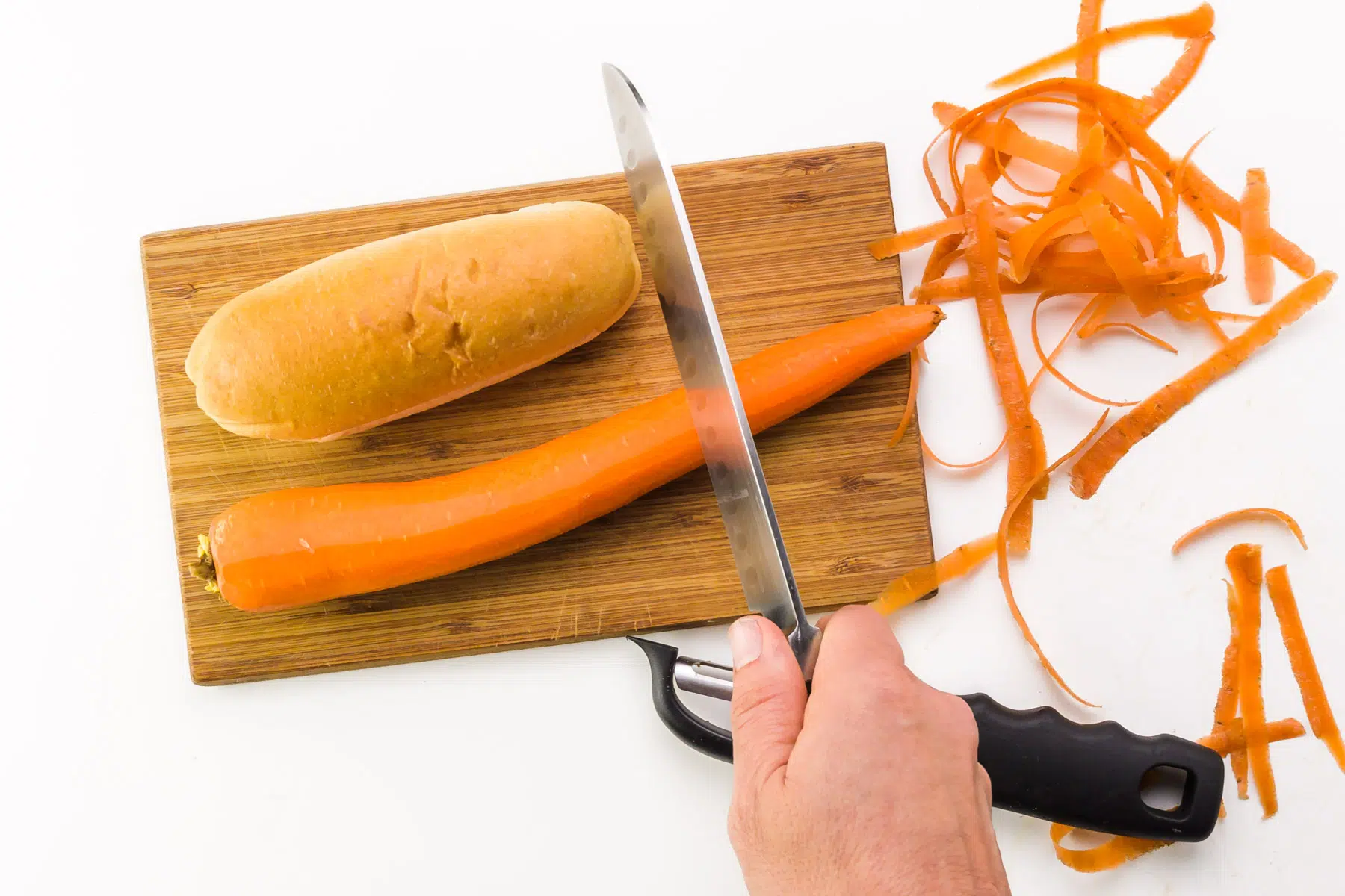 A carrot is being cut to the same length as a hot dog bun. There are carrot shreds and a shredder nearby.
