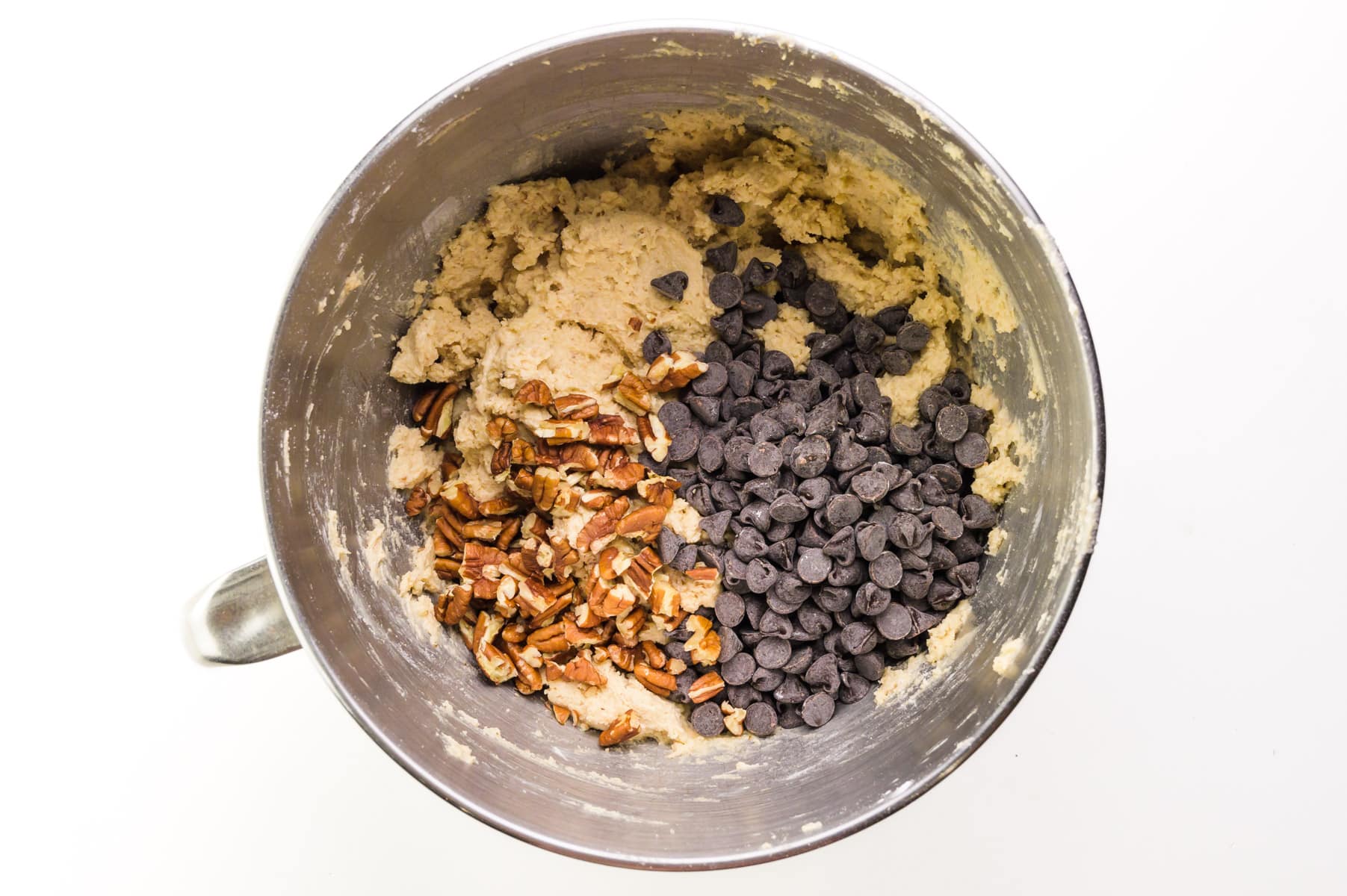 Looking down on a mixing bowl with cookie dough, chocolate chips, and chopped pecans.