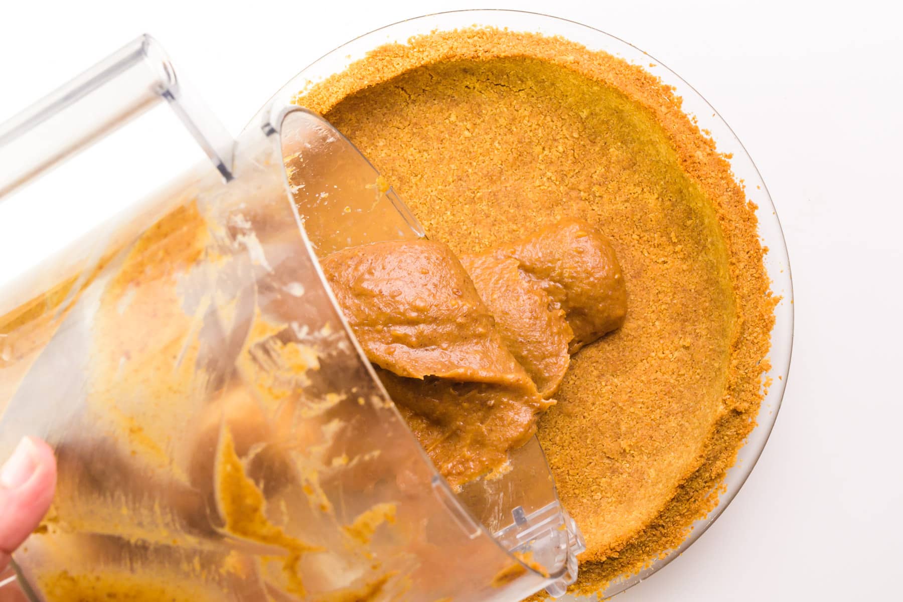 A caramel mixture is being poured from a food processor bowl into a graham cracker crust.