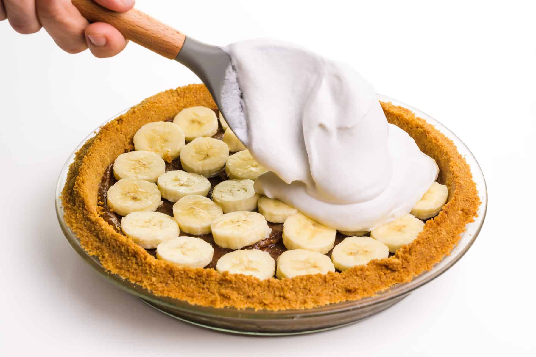 Whipped cream is being spooned over a pie with sliced bananas.