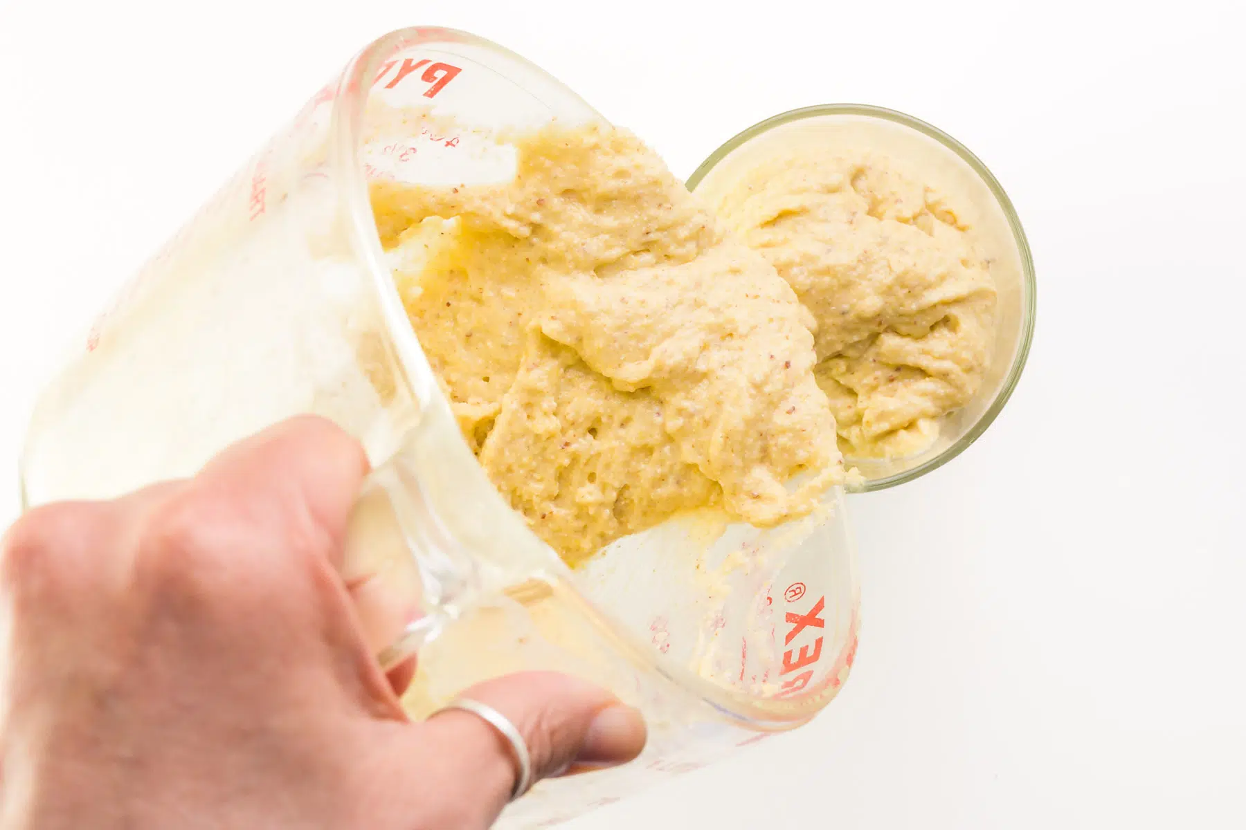 Cornbread batter is being poured from a pyrex measuring cup into tall glass.