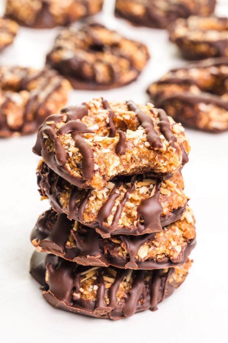 A stack of vegan Samoas cookies with a bite taken out of the top one sits in front of more cookies in the background.