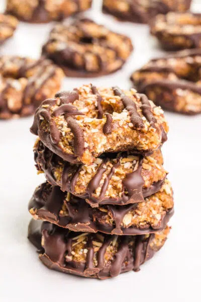 A stack of vegan Samoas cookies with a bite taken out of the top one sits in front of more cookies in the background.