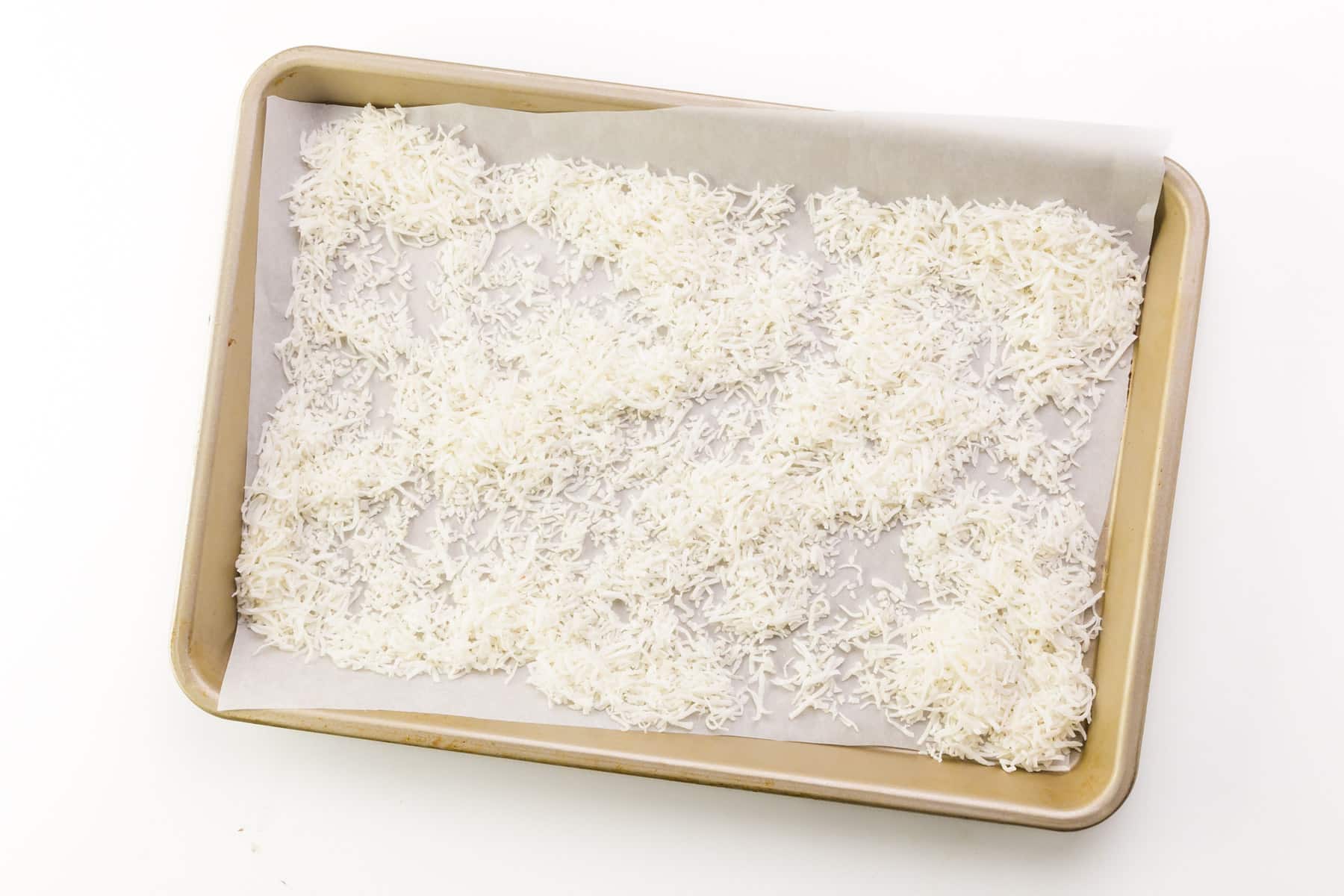 Coconut flakes are lined out in a pan with parchment paper.