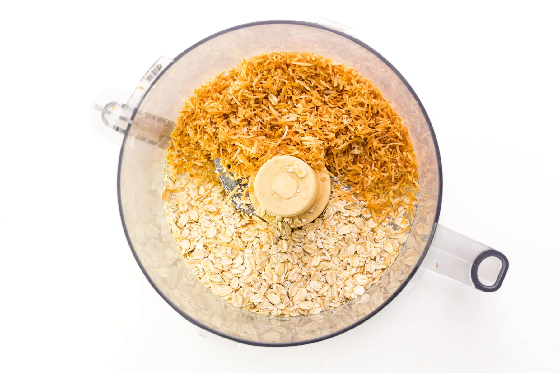 Oats and toasted coconut flakes are in a food processor.