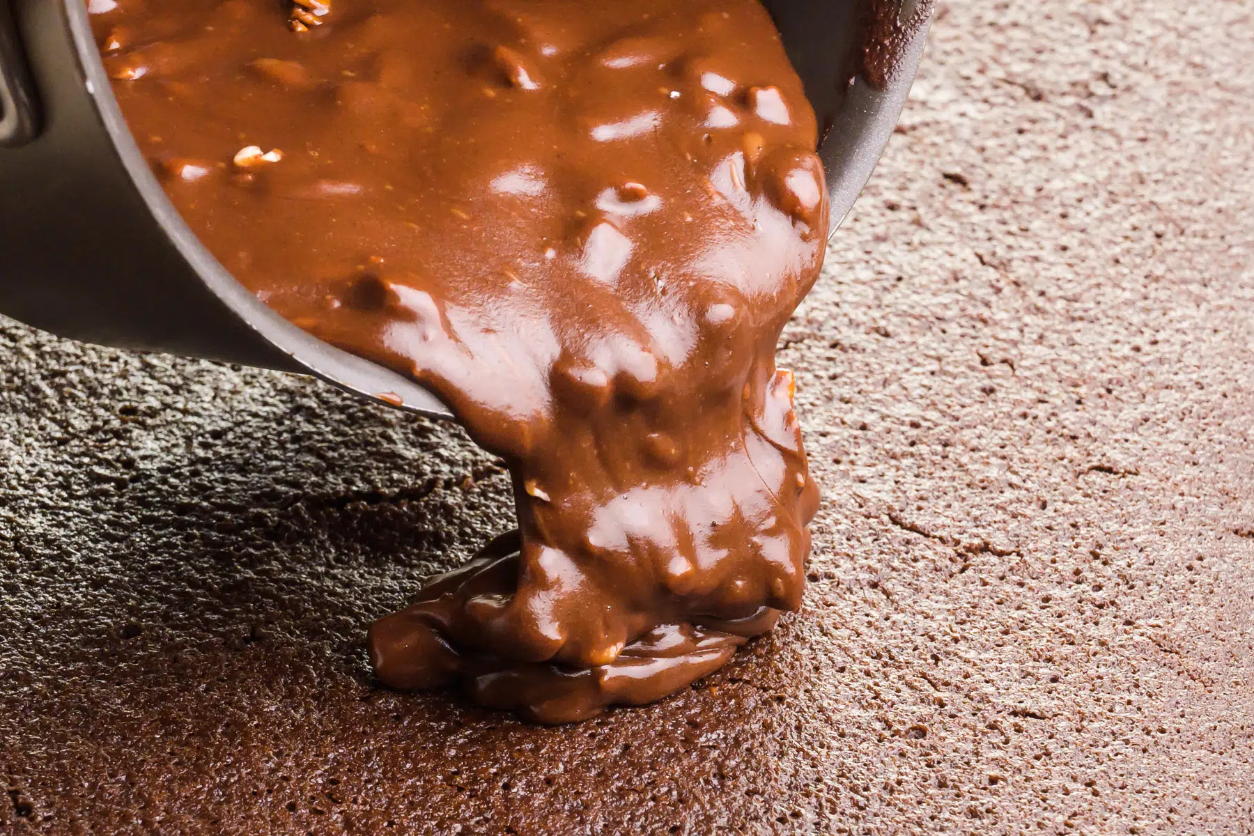 Chocolate frosting is being poured onto a freshly baked chocolate cake.