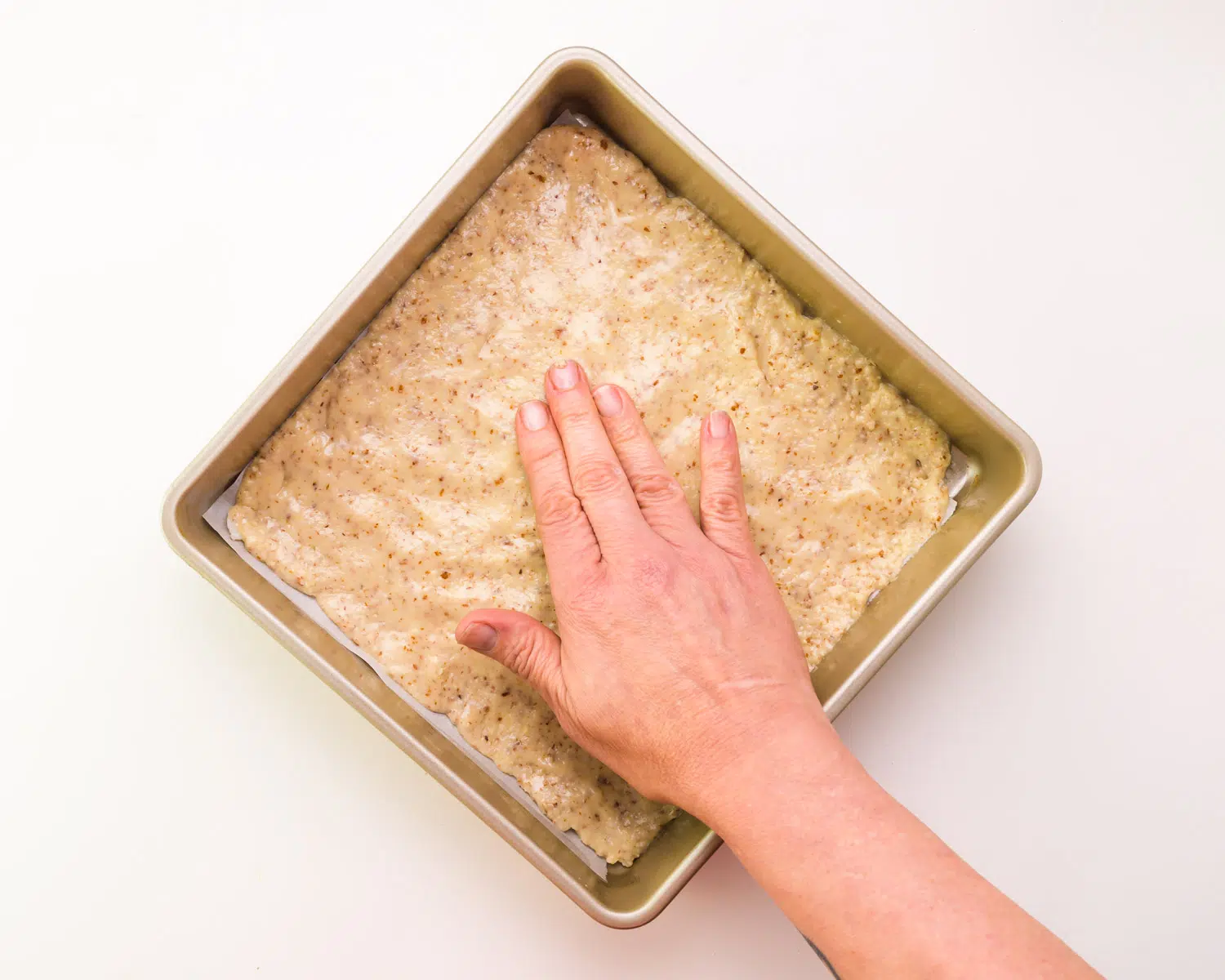 A hand presses batter into a pan.