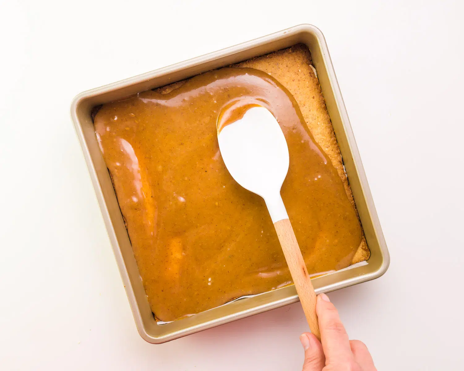 A spatula spreads caramel around in a pan.