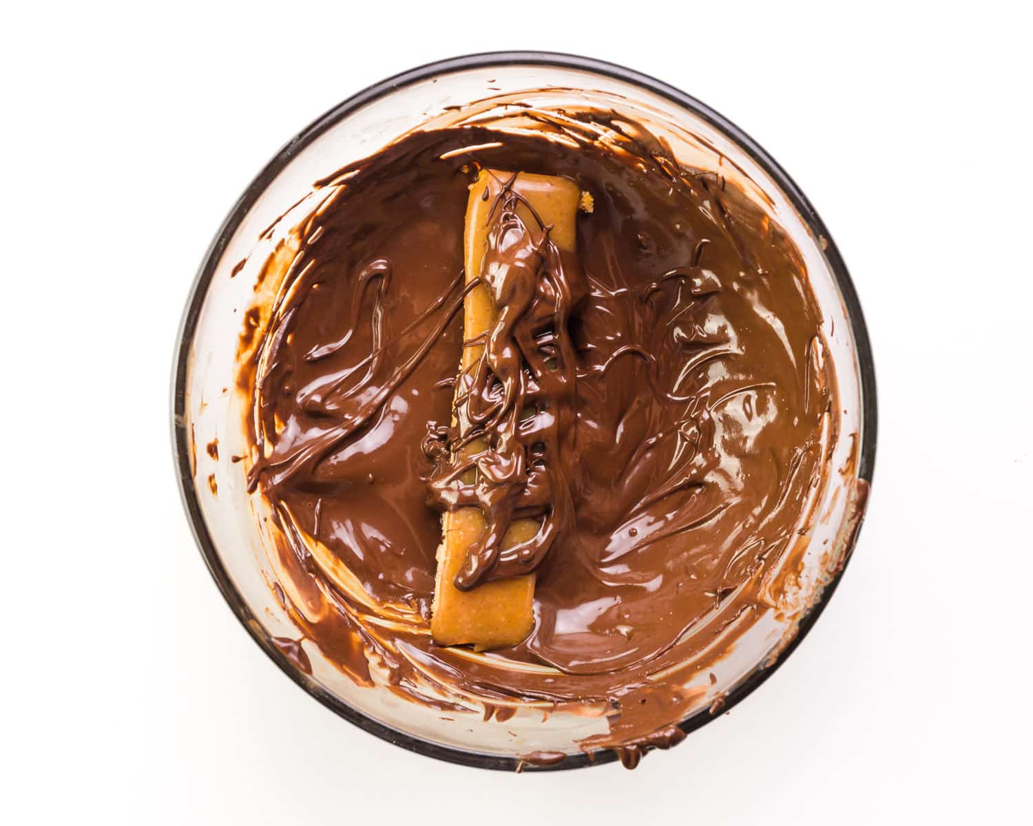 A caramel bar sits in a bowl with melted chocolate, the top of the bar has been drizzled with chocolate.