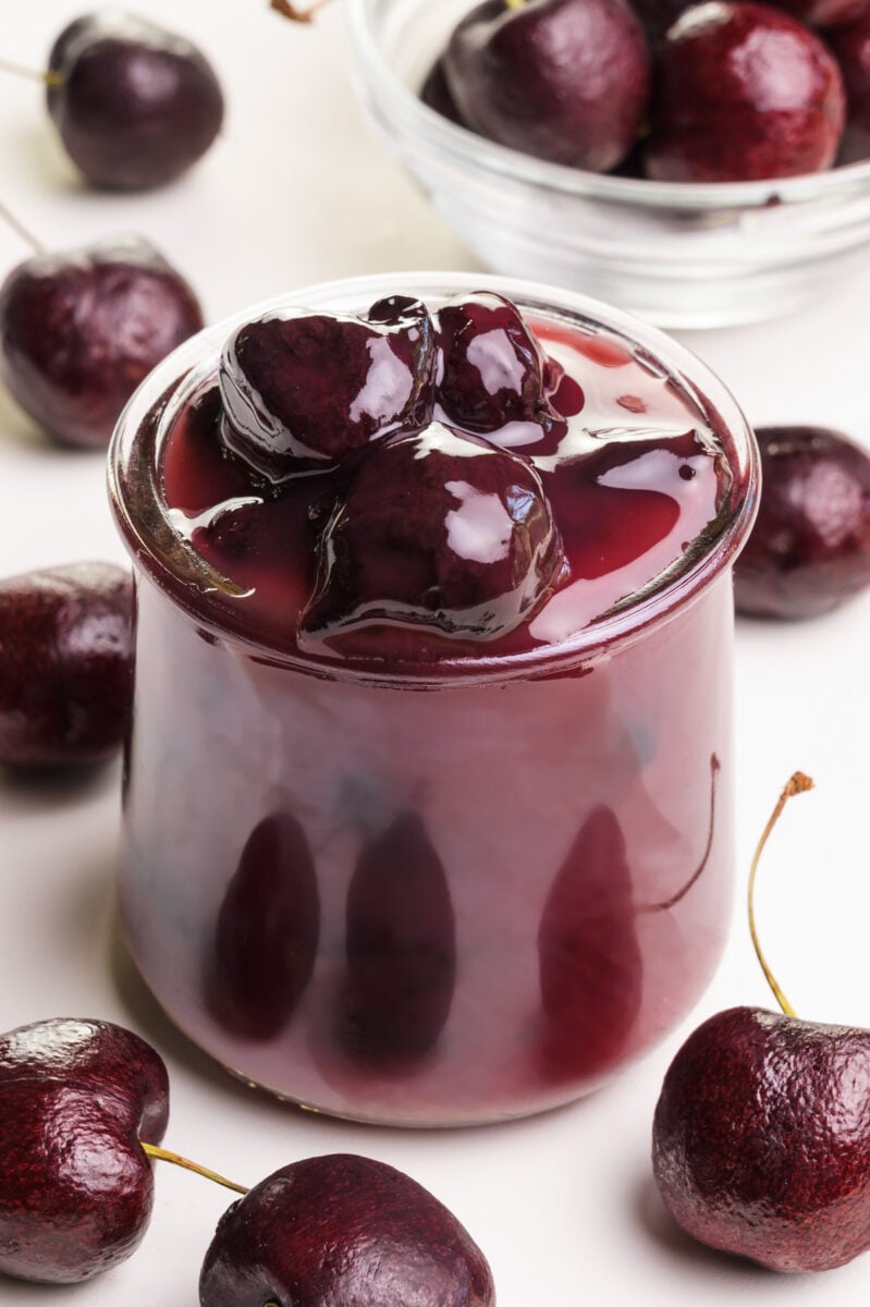 A jar of cherry sauce is surrounded by fresh cherries.