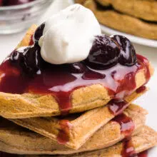 A stack of waffles has cherry sauce and whipped cream on top.
