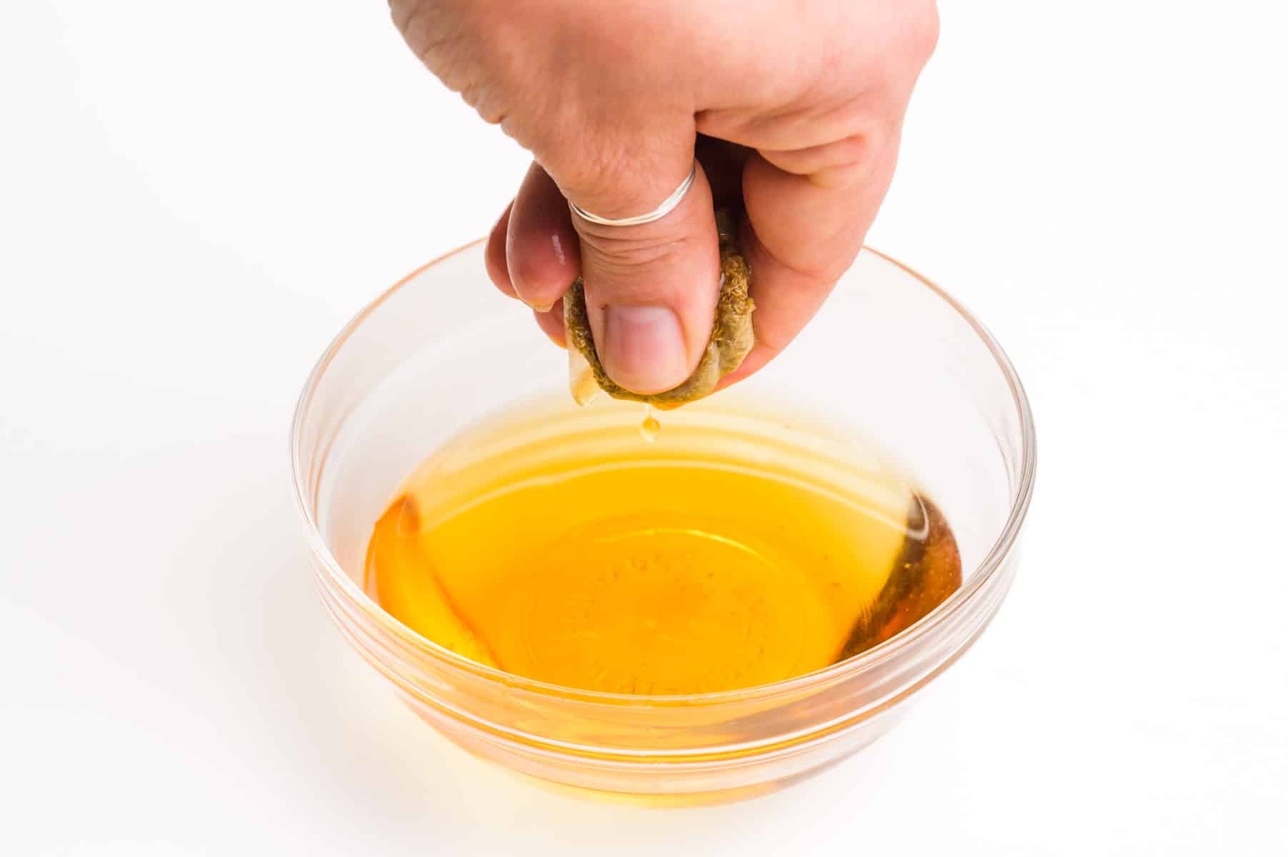 A hand holds a tea bag, squeezing it over a bowl of syrup.