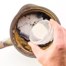 A liquid cornstarch mixture is being poured into a saucepan with a brown sugar mixture.