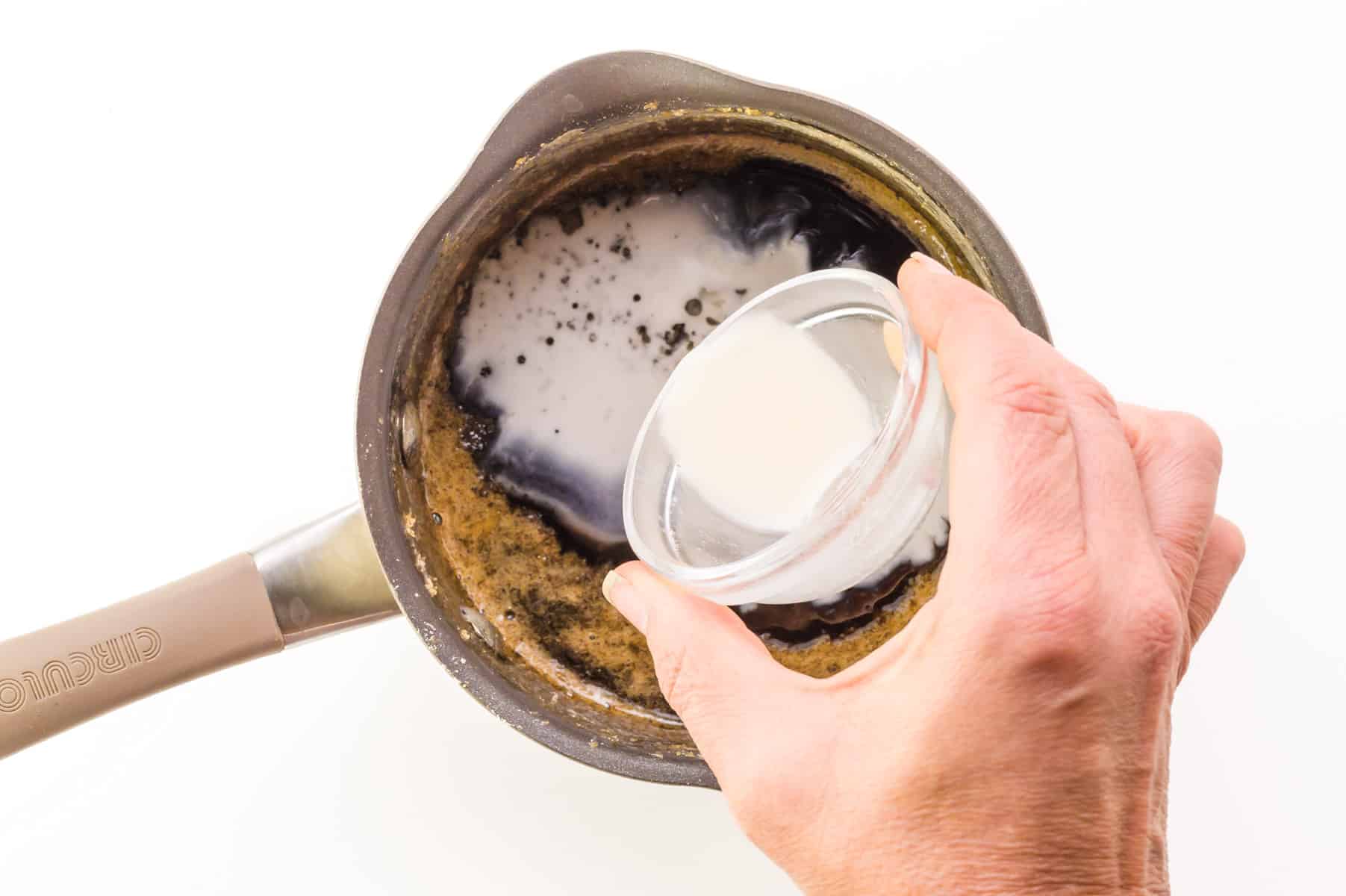 A liquid cornstarch mixture is being poured into a saucepan with a brown sugar mixture.