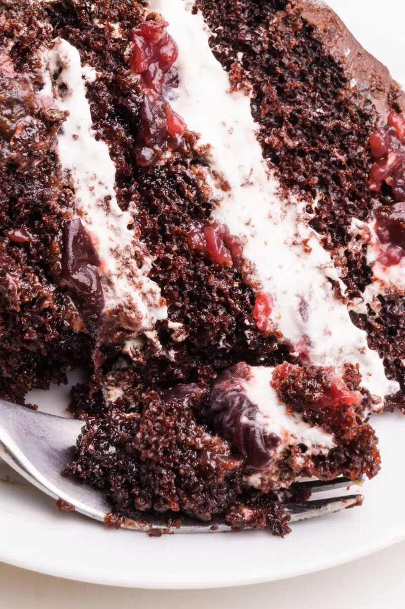 A closeup of a slice of easy Black Forest cake. A bite sits on a fork in front of the cake.