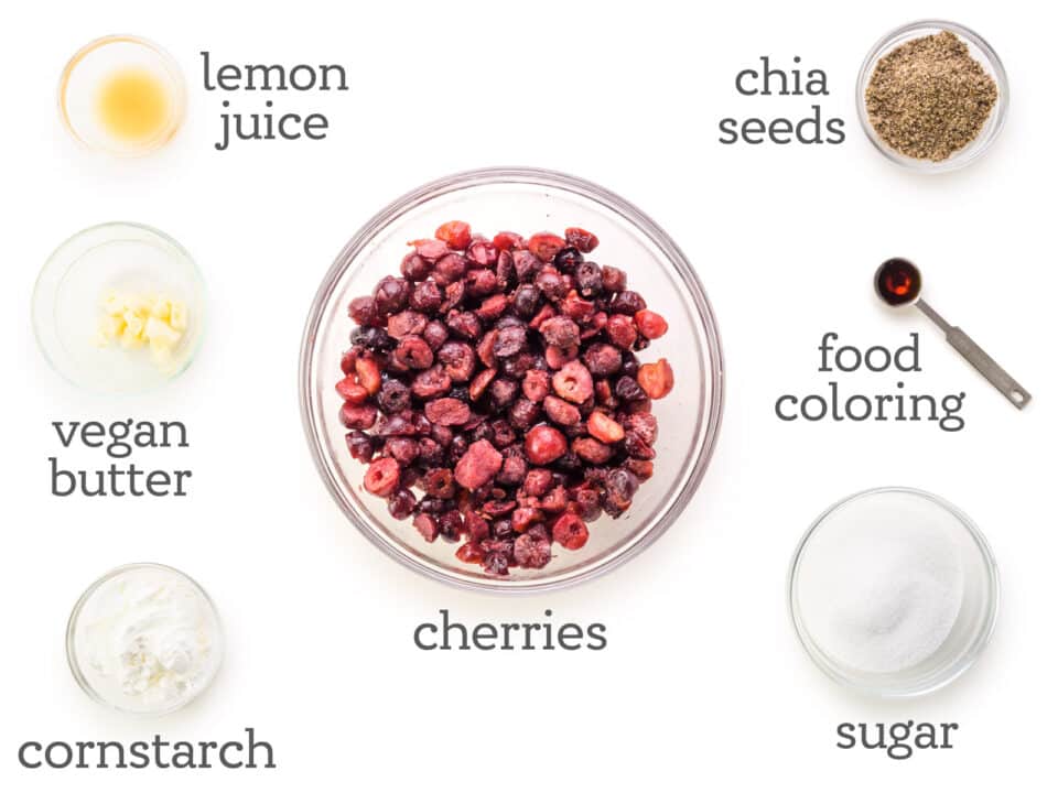 Ingredients are laid out on a white counter. The labels next to them read, chia seeds, food coloring, sugar, cherries, cornstarch, vegan butter, lemon juice.