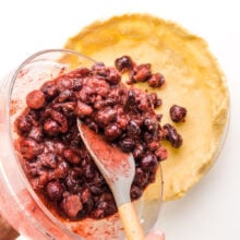 Cherry pie filling is being spooned into an unbaked crust.