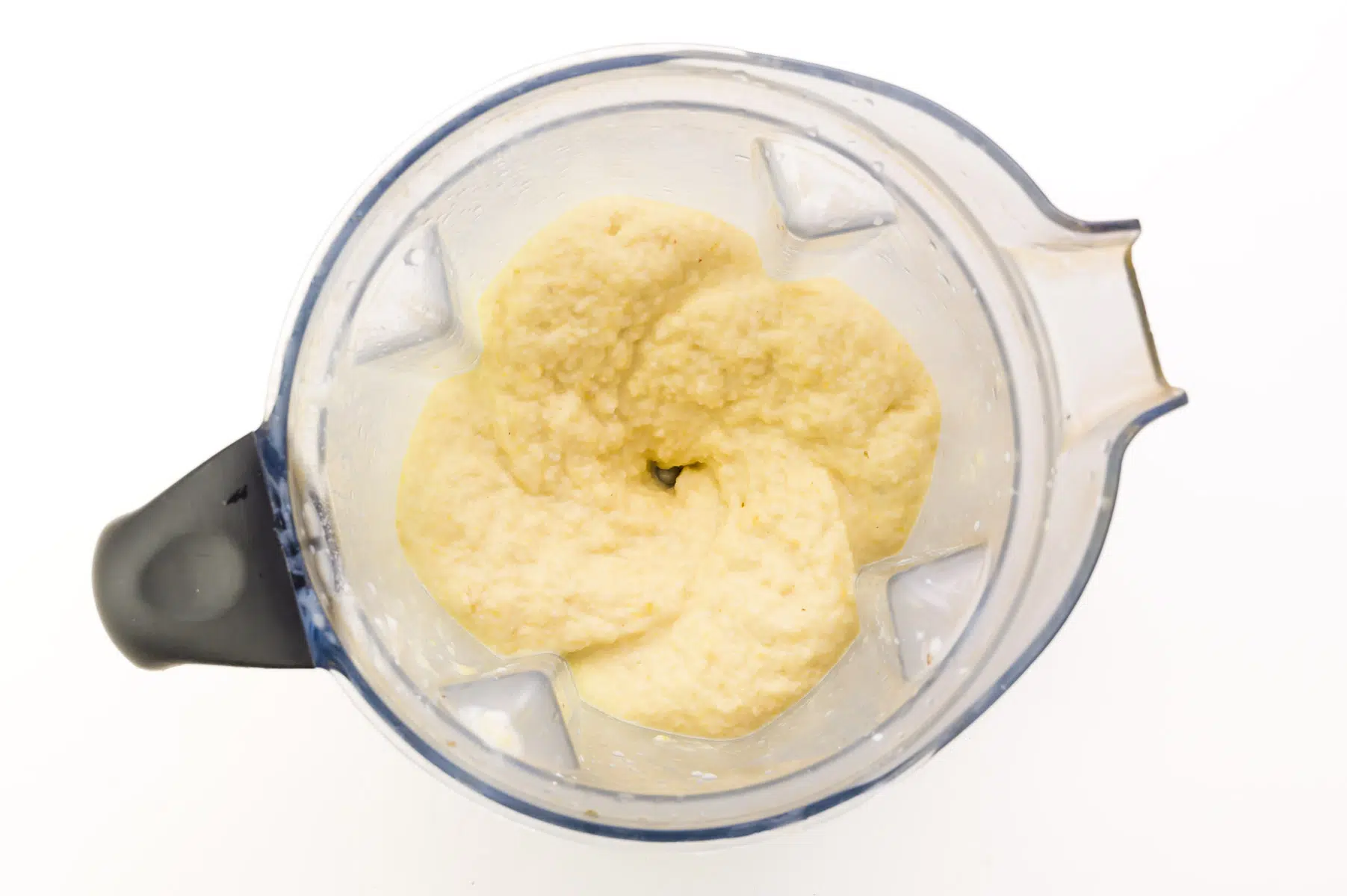 A whipped pineapple mixture is in the bottom of a blender jar.