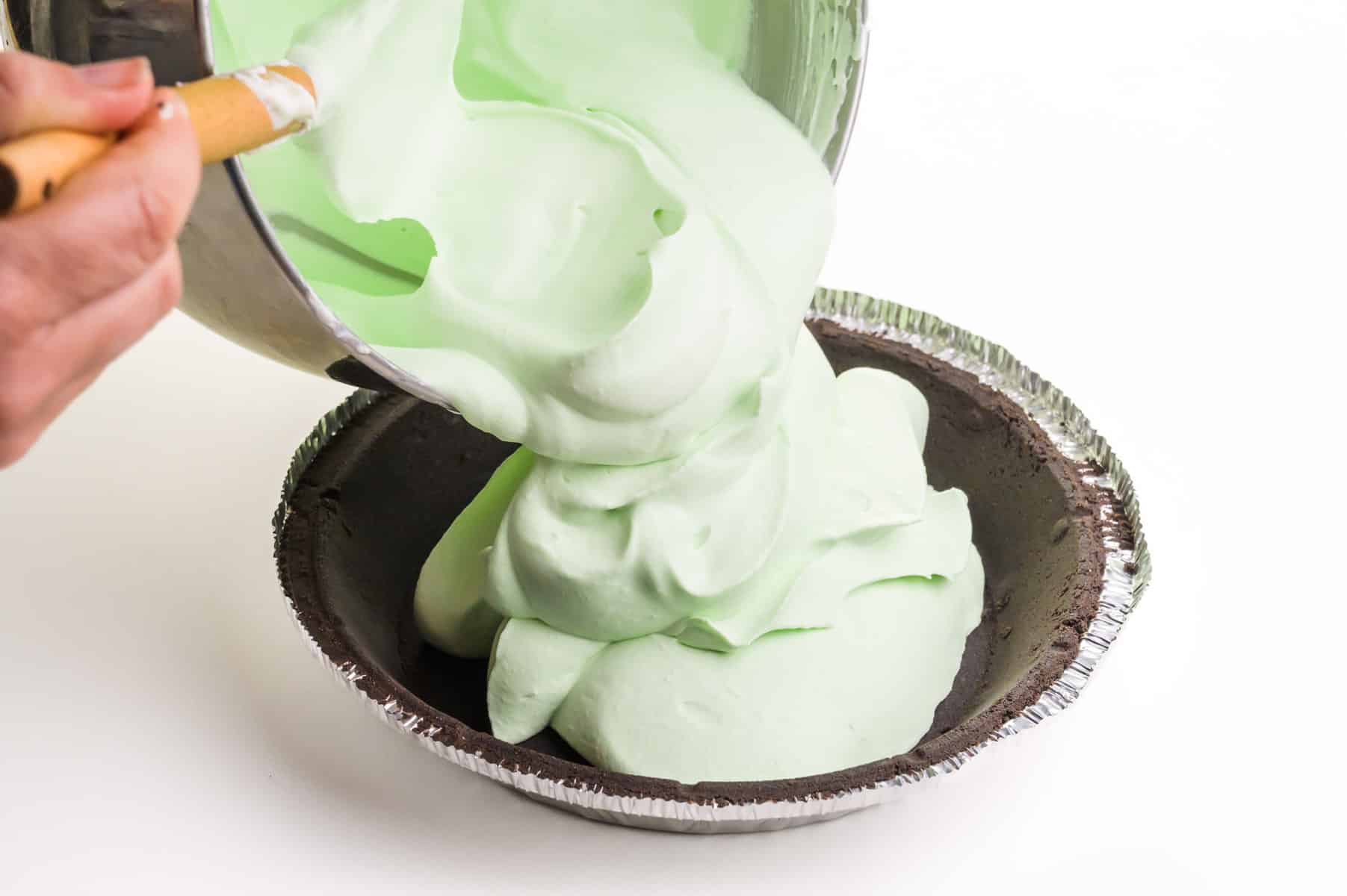 Green whipped mousse being poured into a chocolate pie crust.