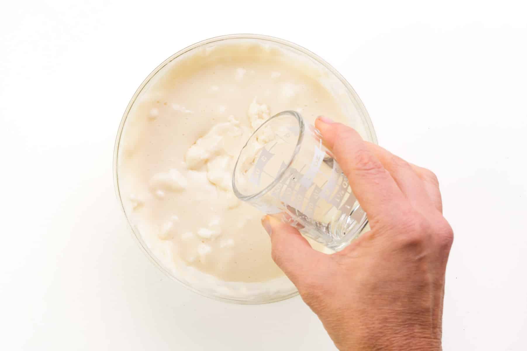 A hand pours crème de menthe into a bowl of melted marshmallows.