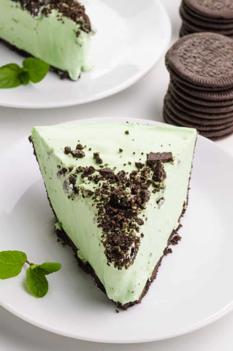 A slice of healthy grasshopper pie sits on a plate.  Another slice on a plate and behind it some chocolate sandwich cookies.