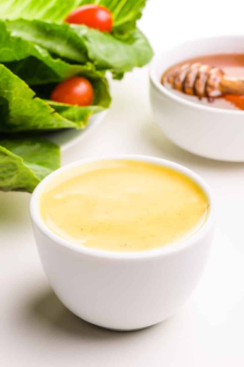 A bowl of egg-free honey mustard sits in front of a salad and a bowl of honey.