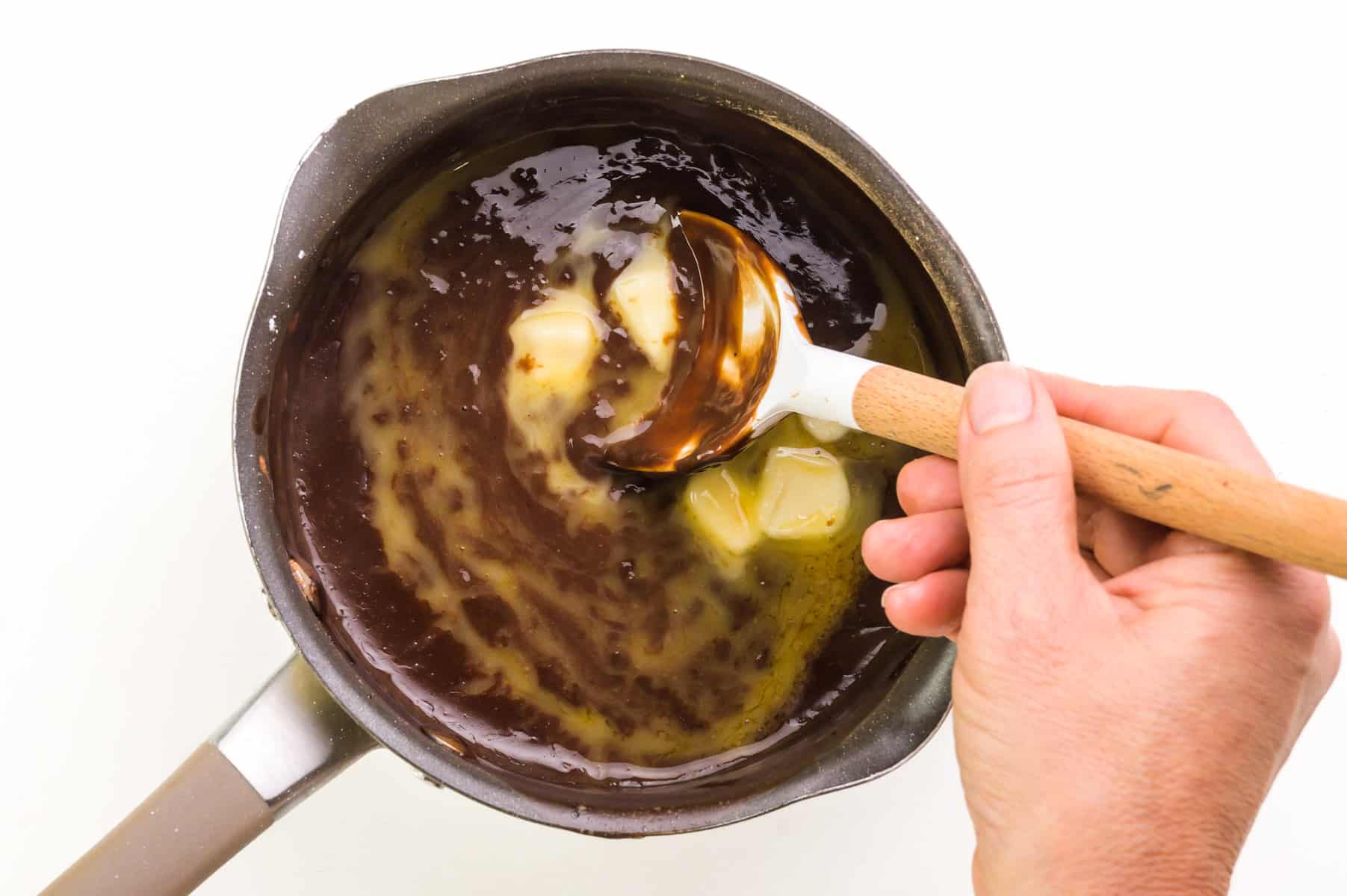 Vegan butter is being stirred into a saucepan with other pudding ingredients.