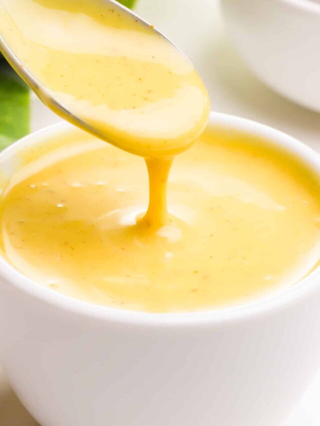 Vegan mustard dressing drizzles from a spoon into a bowl of the sauce.
