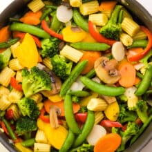 Looking down on a skillet full of veggies, such as green beans, broccoli, carrots, and more.
