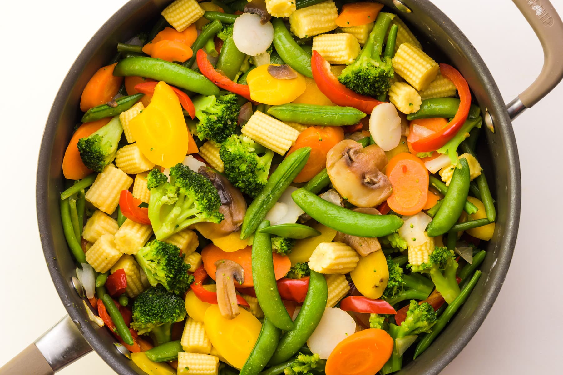 Looking down on a skillet full of veggies, such as green beans, broccoli, carrots, and more.