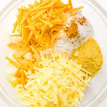 Ingredients like vegan cheese, nutritional yeast flakes, and seasonings are in a bowl.