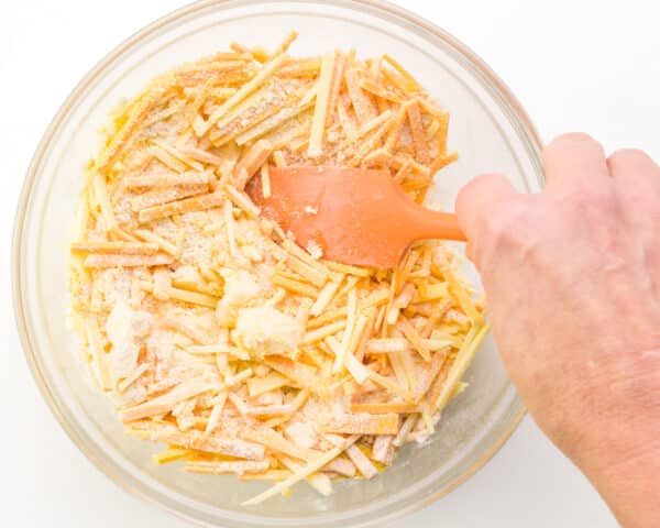 A hand holds a spatula, stirring together a cheese mixture in a bowl.