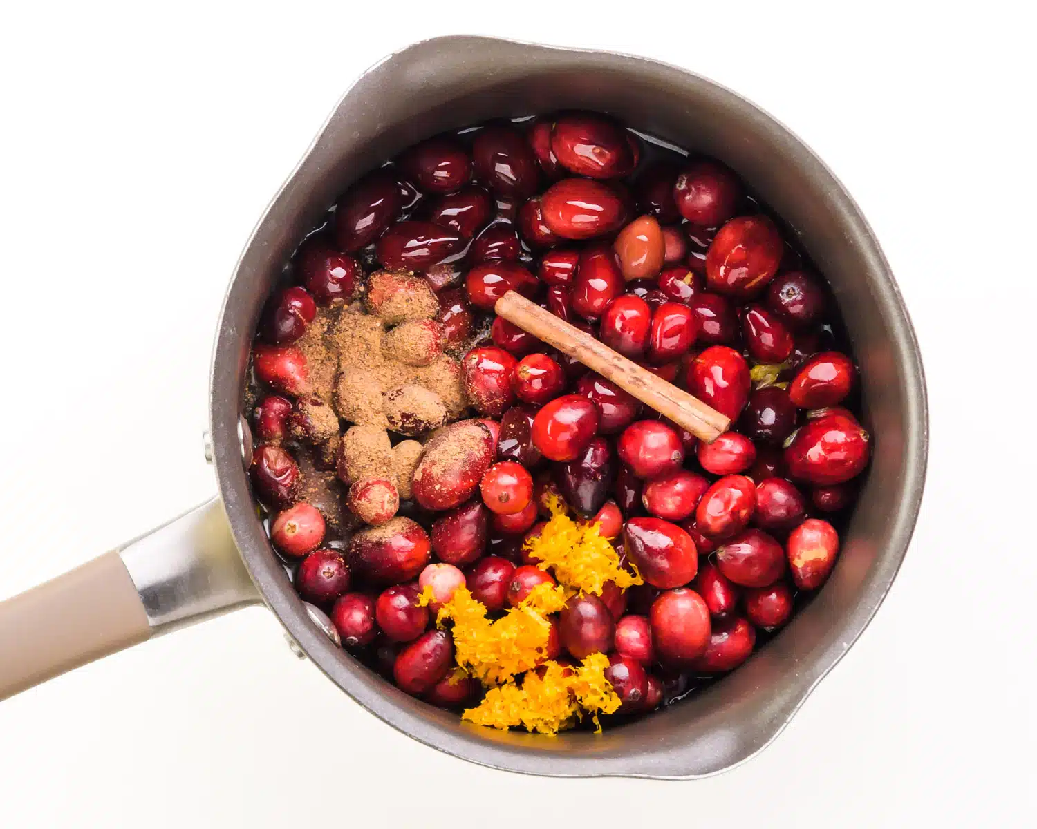 Fresh cranberries are topped with other ingredients in a saucepan.