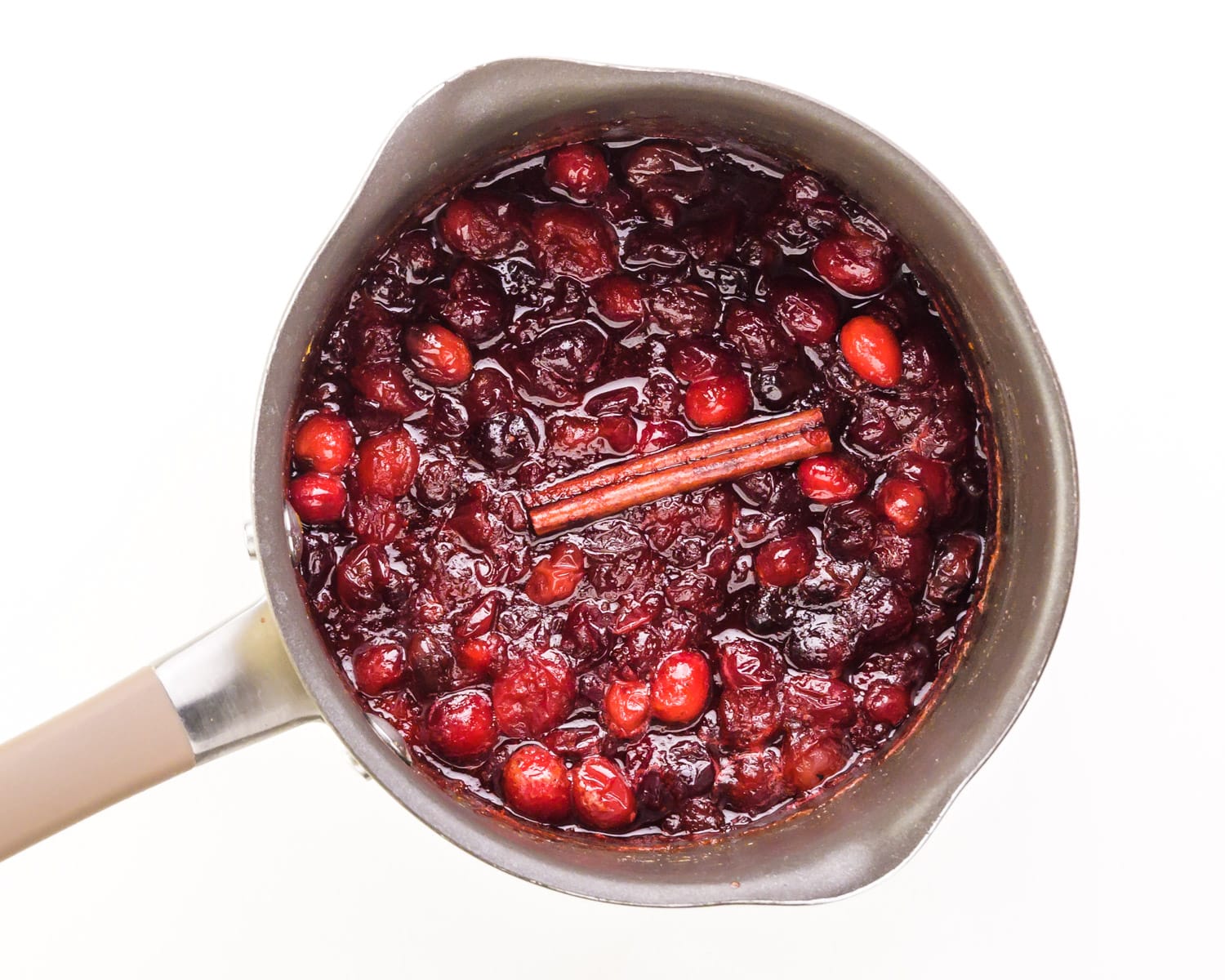 Fresh cranberries are in a saucepan with a cinnamon stick on top.